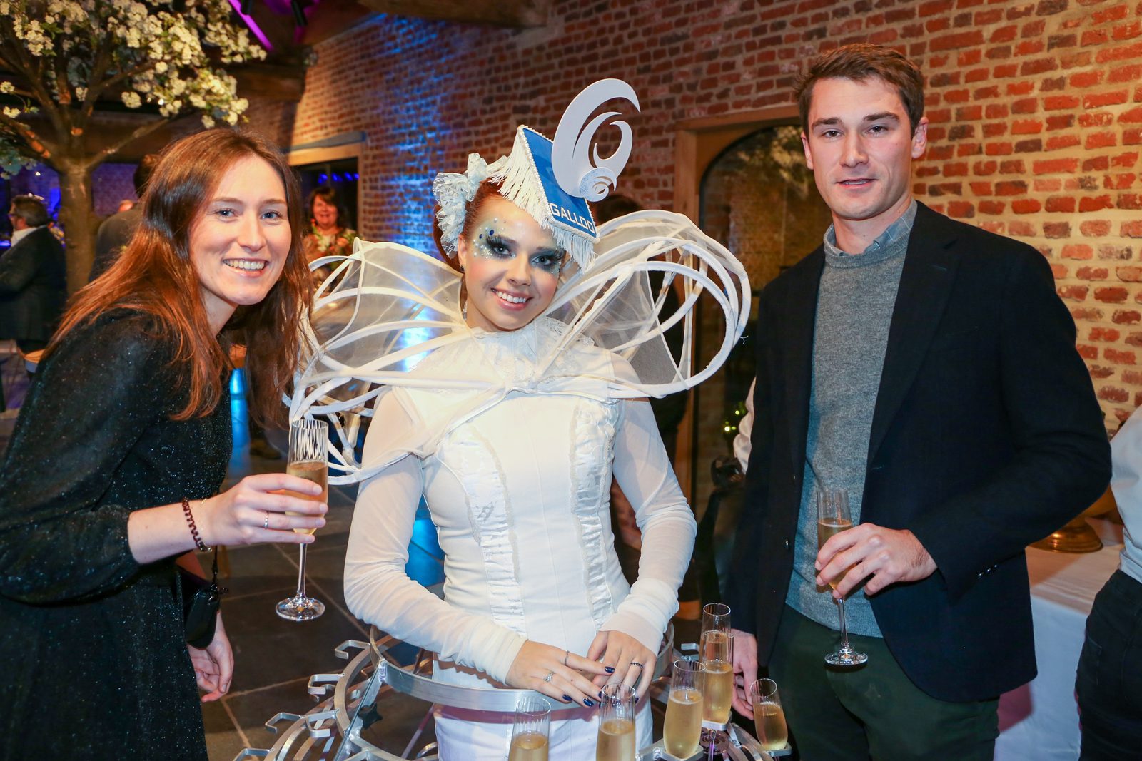 Gasten met champagne naast een hostess in wit kostuum